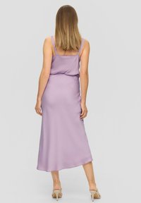Lila satijnen midi-jurk met dunne bandjes, een gladde textuur en een iets vloeiende zoom. Gestyled met naakte hakken met bandjes.