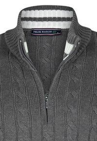 Suéter gris de punto con cuello alto y cierre de cremallera. Presenta un patrón de trenzas y un cuello interior a rayas en blanco y negro.