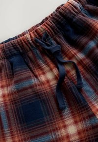 Flannel pajama shorts with a red, blue, and cream plaid pattern. Features an elastic waistband and a navy drawstring. Soft texture.