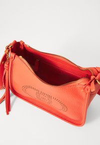 Orange leather crossbody bag with textured surface, gold hardware, dual zip compartments, and decorative perforated design on the front.