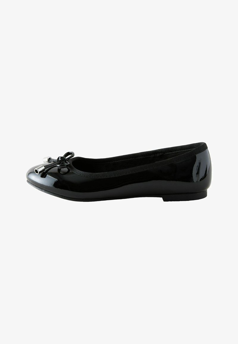 Ballerine en cuir verni noir avec bout arrondi, talon bas et nœud décoratif à embouts métalliques sur fond blanc.
