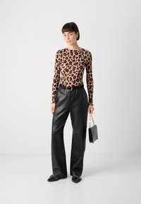 Langermet topp med leopardmønster, kombinert med høyt liv og vide svarte lærbukser. Tilbehøret inkluderer en liten svart håndveske med kjedesnor.