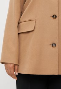 Τα καφέ παλτό από μείγμα μάλλινου υφάσματος με δομημένη σιλουέτα, που διαθέτει τσέπη στο στήθος, κουμπιά για κλείσιμο και απαλό, λείο υφή.