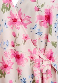 Zwiewna sukienka kopertowa z miękkiego, lekkiego materiału. Ozdobiona dużymi różowymi i niebieskimi kwiatami na jasnym tle, z detalem w postaci przewiązanego w talii paska.