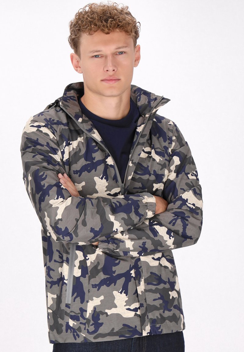 Giacca mimetica in grigio, blu navy e crema, con chiusura a zip frontale, colletto alto, polsini elastici e due tasche laterali. Materiale leggero.