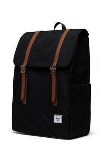 Black canvas backpack featuring brown leather straps and silver hardware, square shape, top flap, and a front label patch.