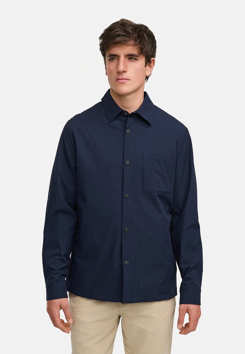 Mörkblå knäppt jacka i lätt tyg, med en bröstficka, spetsig krage och långa ärmar. Slät textur.