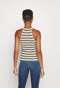 Top de tirantes a rayas beige y negro con un diseño ajustado y estilo racerback, combinado con jeans de mezclilla azul, visto desde atrás.