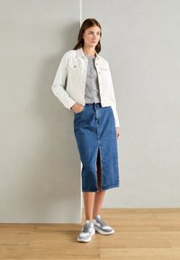 White denim jacket, gray striped top, blue maxi skirt with front slit, and gray sneakers. Minimalist design with subtle hardware accents.