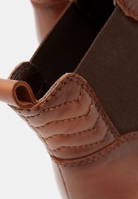 Ruskeat nahkaiset nilkkurit, joissa kangaspaneeli, ompeludetaljit ja kantapäässä vetokahva helppoa pukemista varten.