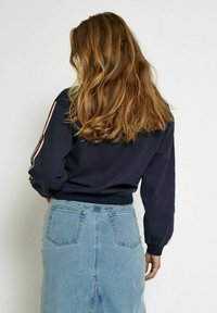 Navy sweatshirt with red and white side stripes, ribbed cuffs, paired with a light blue denim skirt featuring pockets and a slight slit.