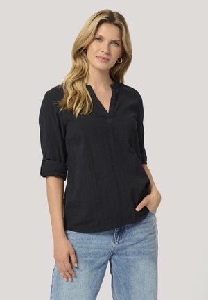 Black collared blouse with rolled sleeves and subtle vertical stripes. Paired with light blue jeans, showcasing a relaxed fit and texture.