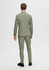 Light green suit with tailored design, featuring a single vent back and matching trousers. Black footwear completes the look.