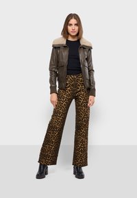 Brun läderbomberjacka med beige fuskpälskrage, kombinerad med leopardmönstrade utsvängda byxor. Modellen bär en svart topp och plattformskängor.