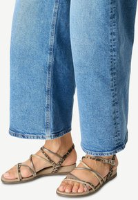 Sandali piatti con più cinturini in bronzo metallizzato e stampa animale. Abbinati a pantaloni in denim azzurro chiaro, larghi e risvoltati alla caviglia.