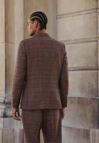 Brown checkered suit with a tailored fit. The blazer features a notch lapel and buttoned cuffs. Subtle texture enhances the fabric's appearance.