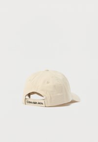 Μπεζ βαμβακερό καπέλο μπέιζμπολ με κυρτή γείσο, ρυθμιζόμενο λουράκι στο πίσω μέρος και λογότυπο "Calvin Klein Jeans" στο λουράκι.
