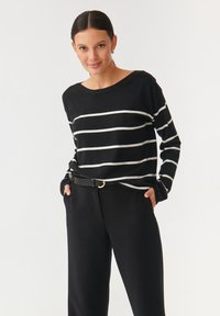Top lung cu dungi negre, dintr-un material moale, cu dungi orizontale albe, croială lejeră și guler rotund, asortat cu pantaloni negri cu talie înaltă.