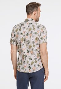 Camisa de manga corta en beige claro con un patrón floral que incluye hojas verdes y flores naranjas y moradas. Dobladillo recto y cuello.