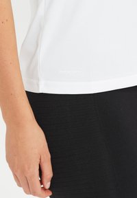 Vit snabbtorkande topp med en slät textur, kombinerad med svarta åtsittande leggings med ribbad design och en neutral färgpalett.