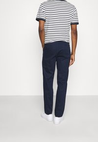 Marinblå byxor med rak passform, kombinerat med en randig kortärmad skjorta och vita sneakers; synliga bakfickor.