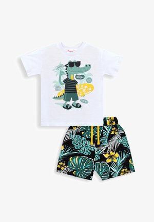 Hvid kortærmet skjorte med tegneserie-krokodille i solbriller og surfbræt, kombineret med sorte blomstrede shorts med grønne og gule tropiske blade.