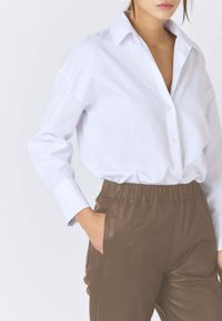 Witte katoenen overhemd met knopen en kraag, gedragen met bruine broek met elastische tailleband, met een gladde textuur en een ontspannen pasvorm.