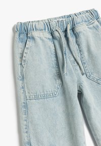 Pantaloni in denim azzurro chiaro con vita elastica, cordoncino e due tasche frontali. Il tessuto ha una texture morbida con aree sbiadite.