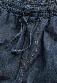 Tumed sinised denim lühikesed püksid, millel on kogutud elastne vöökoht, reguleeritav nöör ning nähtavad kollased õmblusteed.