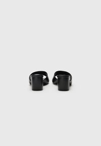 Schwarze Mules mit offener Ferse aus glattem Leder, ausgestattet mit einem kurzen Blockabsatz und minimalistischen Design. Geeignet für legere oder formelle Anlässe.