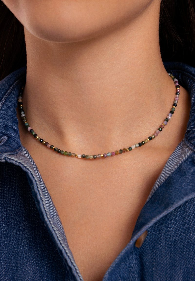 Collana di perline colorate con piccole pietre preziose multicolori dal texture liscia e lucida, appoggiata su un colletto di denim.
