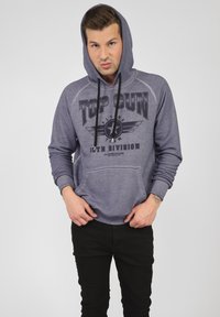 Grå hoodie med frontficka, prydd med grafiskt tryck "TOP GUN" och stjärninsigne. Svarta snören, ribbade muddars och nederkant.