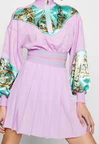 Lila klänning med en figursydd bodice, plisserad kjol och teal satinprydnader med gyllene utsmyckningar, dragkedjestängning och märkeselastisk midjeband.