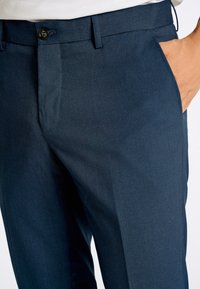 Mörkblå dressbyxor med slät framkant, sidfickor och knappstängning, tillverkade av mjukt, strukturerat tyg.