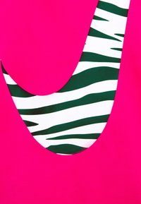 Gros plan sur un tissu rose vif avec une découpe courbe révélant un motif rayé zèbre blanc et vert foncé en dessous.