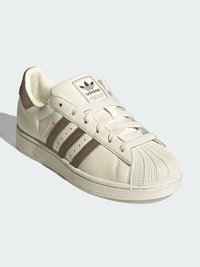 Biela kožená teniska s hnedými semišovými detailmi, troma vodorovnými pruhmi a štruktúrovanou gumovou špičkou. Na jazyku je klasické logo.