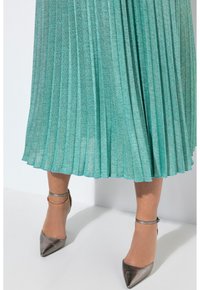 Gonna plissettata fino al ginocchio in tessuto turchese chiaro con riflessi metallici. Tacchi grigi a punta con cinturini alla caviglia completano il look.