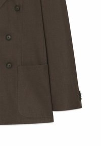 Manche et devant de blazer marron avec boutons noirs et grande poche rectangulaire sur fond blanc.
