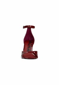 Sandale à talon haut en cuir verni rouge avec une bande de cheville, design à bout ouvert et intérieur texturé. Logo noir imprimé sur la semelle intérieure.