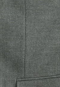 Grau strukturierter Stoff mit einem gewebten Muster, der eine vertikale Naht und ein Taschendetail am unteren Ende aufweist.
