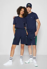 Navy katoenen t-shirts en shorts, beide met groene accenten, gecombineerd met witte sneakers en meerkleurige gestreepte sokken, met kleine merkl logo's.