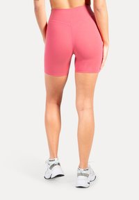 Roze, hoog uitlopende, nauwsluitende shorts met een gladde textuur en gestikte naden, gecombineerd met witte sportschoenen.