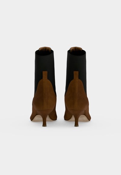 Paire de bottines en daim marron et cuir noir avec talons kitten vue de dos sur fond blanc.