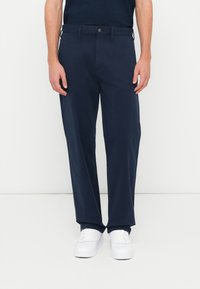 Navy-blauwe katoenbroek met een rechte pasvorm, voorzien van een knoopsluiting aan de voorkant, riemlussen en zijzakken. Gecombineerd met witte sneakers.