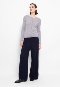 Cardigan in lana grigia con maniche lunghe, scollatura rotonda e chiusura con bottoni, abbinato a pantaloni larghi blu scuro e scarpe nere.