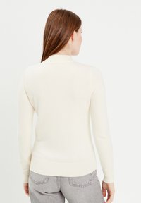 Pull blanc ajusté avec un col montant et des manches longues. Il dispose d'un ourlet et de poignets côtelés. Le matériau semble doux, avec une texture lisse.
