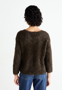 Brauner, flauschiger Pullover mit weicher Textur, weit ausgeschnittenem Ausschnitt und Dreiviertelärmeln, kombiniert mit blauen Jeans.