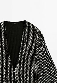 Czarny i biały kardigan w pionowe paski z dwoma białymi guzikami i głębokim kołnierzem w kształcie V na jednolitym tle.