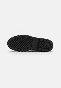 Black rubber shoe sole with a textured, ridged pattern and a wider heel portion for stability. Includes embossed brand lettering.