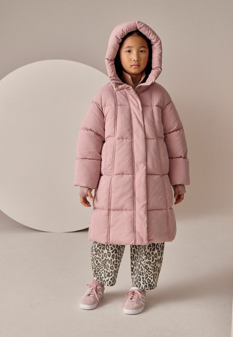 Lyserød polstret jakke med hætte, prydet med quiltede linjer; parret med leopardmønstret bukser og lyserøde sneakers. Neutral baggrundsaccenter.